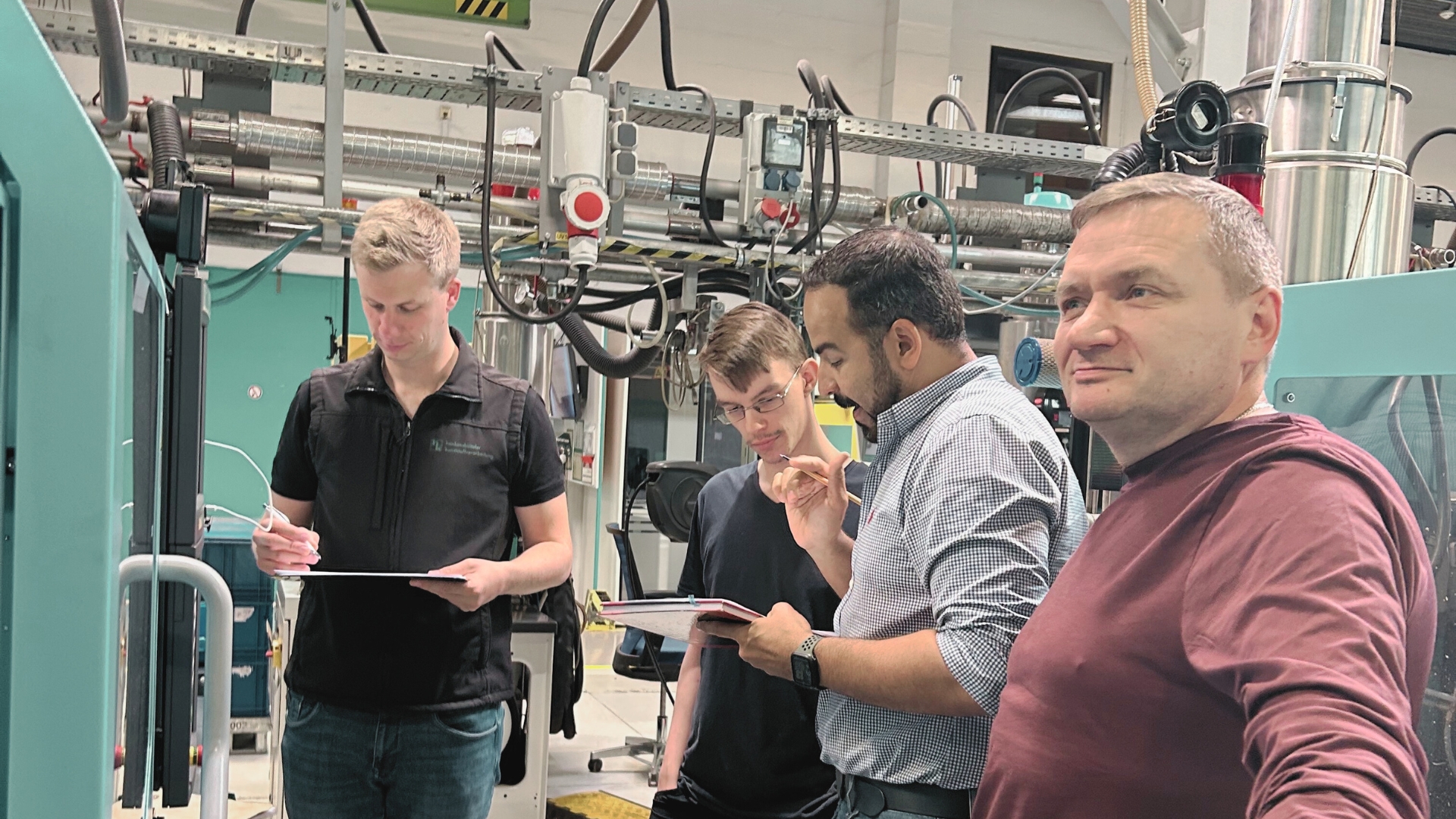 Ein Team aus Einrichter, Produktionsleitung und QS-Leitung führt in der Fertigung von hk ein Maschinenaudit an einer Spritzgießmaschine durch – gemeinsamer Einsatz für Qualität und Prozesssicherheit.